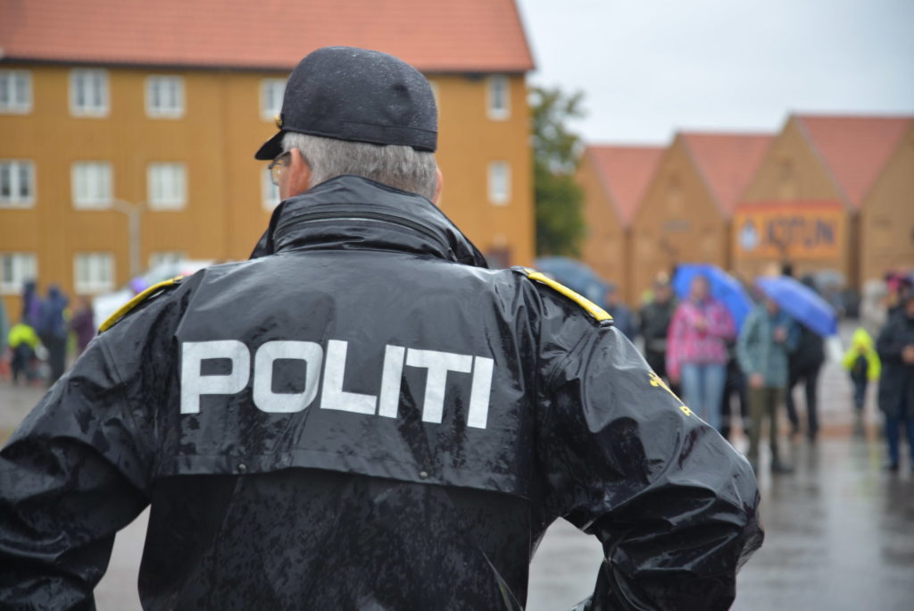 Politimann står med ryggen til kamera med en jakke med teksten POLITI. Foto.