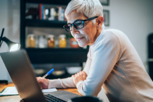 Eldre dame lener seg over en bærbar datamaskin, og ser tenkende ut. Foto